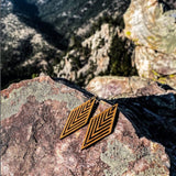 Geometric diamond wooden earrings on a rock in the mountain side.