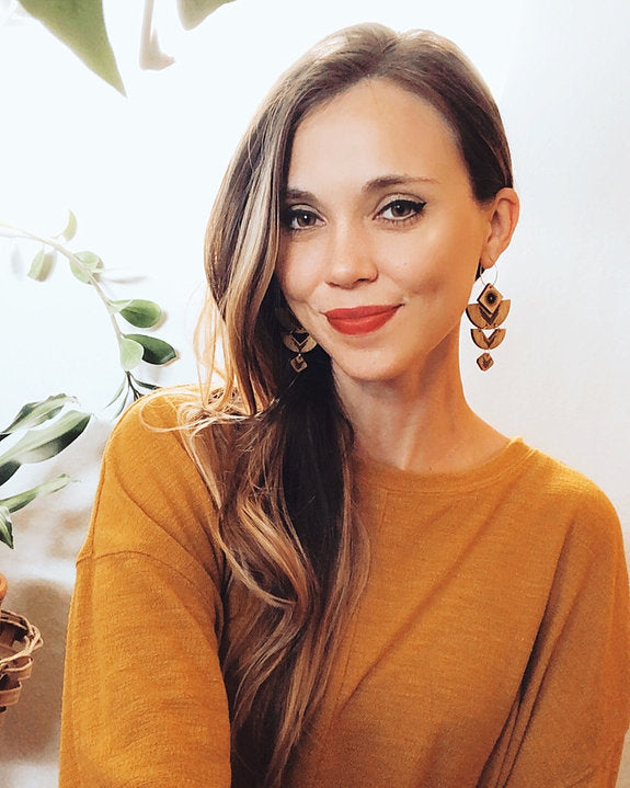 Smiling woman wearing wooden geometric earrings and a orange sweater.