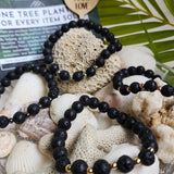 Four lava stone bracelets resting along shells and beach rocks, with a palm leaf and 'lovelevel' card in the background.