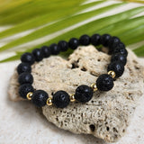 Lava stone bracelet resting along a heart shaped stone with a palm leaf in the background.