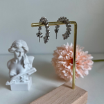 Silver hoop earrings draped over a gold bar with a statue and pink flower in the background.