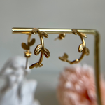 Golden hoop earrings hanging from a golden bar against a blurred background