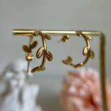 Golden hoop earrings hanging from a golden bar against a blurred background