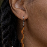 Close up of an ear with a wooden dangle earring and braided hair.