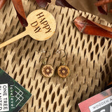 Wooden dangle earrings with a sun design against a natural background with a 'Happy Day' plant marker.