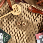 Wooden stud earrings with a sun design against a natural background with a "Happy Day" plant marker.