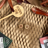 Wooden stud earrings with a sun design against a natural background with a "Happy Day" plant marker.
