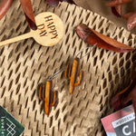 Wooden cactus earrings on a natural background with dried leaves and a "Happy Day" plant marker.