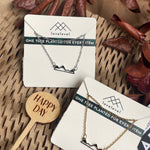 Mountain peak necklaces on cards with 'lovelevel' branding against a natural background.