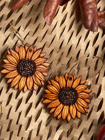 Wooden sunflower earrings on a textured surface with dried leaves.