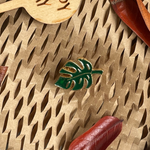 Gold and green enamel Monstera pin on a natural background.