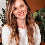 Smiling women in knitted sweater wearing wooden earring against office background.
