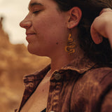 Woman wearing wooden snake earrings with a blurred natural background