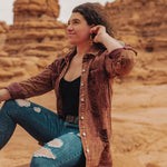 Woman sitting on a rock in a desert landscape with red rock formations.