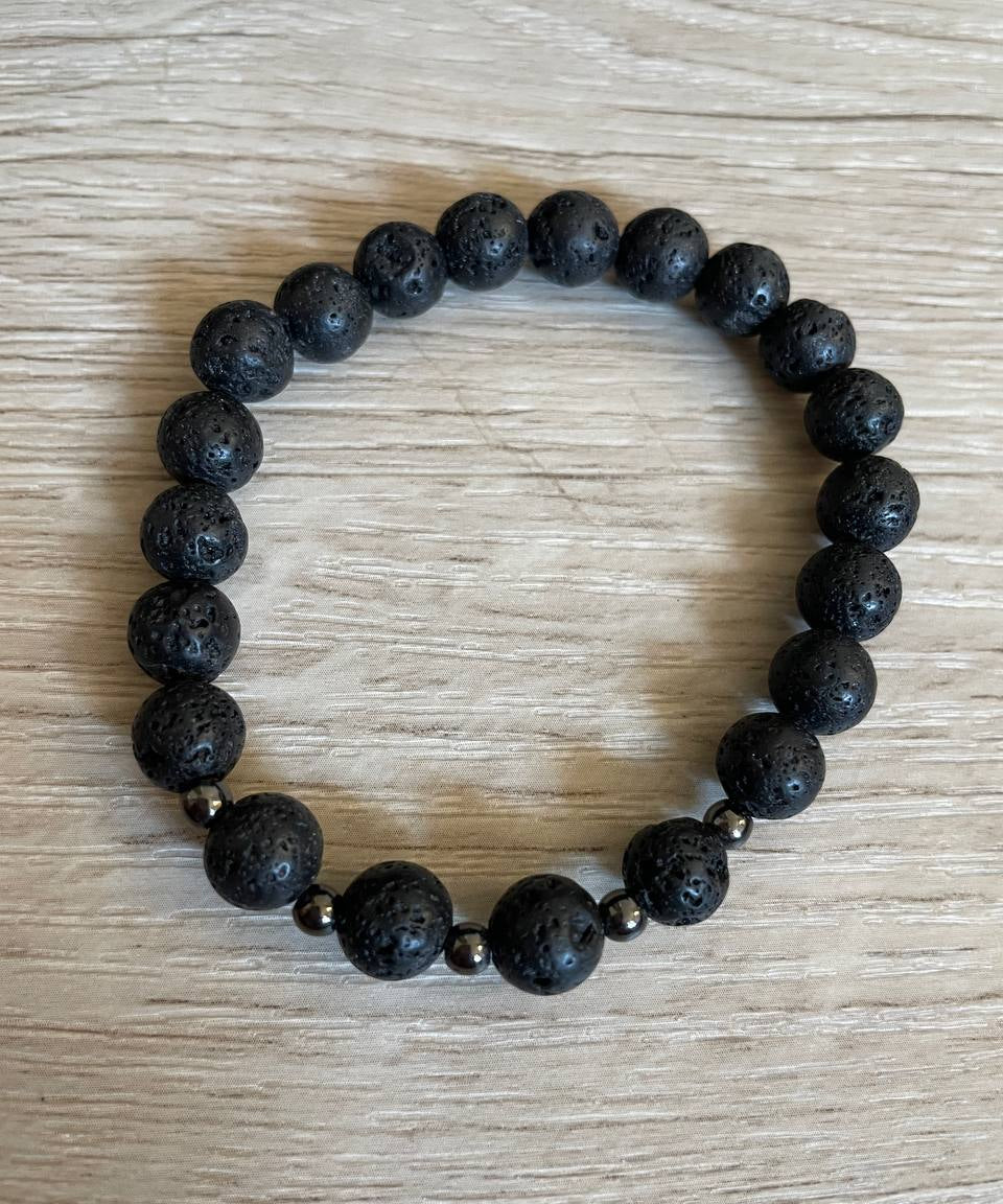 Lava stone bracelet with 5 black metal beads against a wooden background.