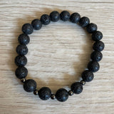Lava stone bracelet with 5 black metal beads against a wooden background.