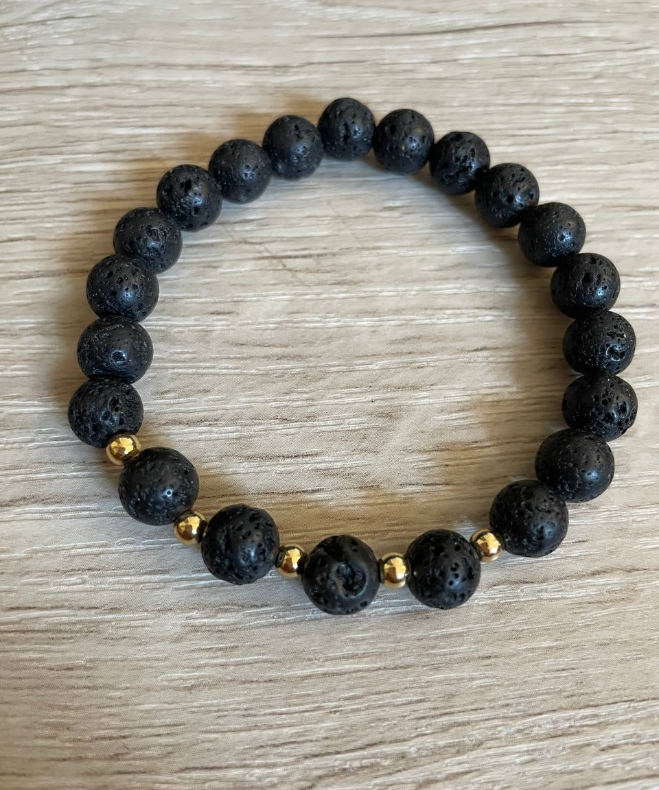 Lava stone bracelet with 5 gold beads against a wooden background.