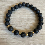 Lava stone bracelet with 5 gold beads against a wooden background.