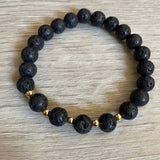 Lava stone bracelet with 5 gold beads against a wooden background.