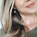 Smiling blond woman wearing a wooden dangle earring with a bright blue stone in the center of the earring.