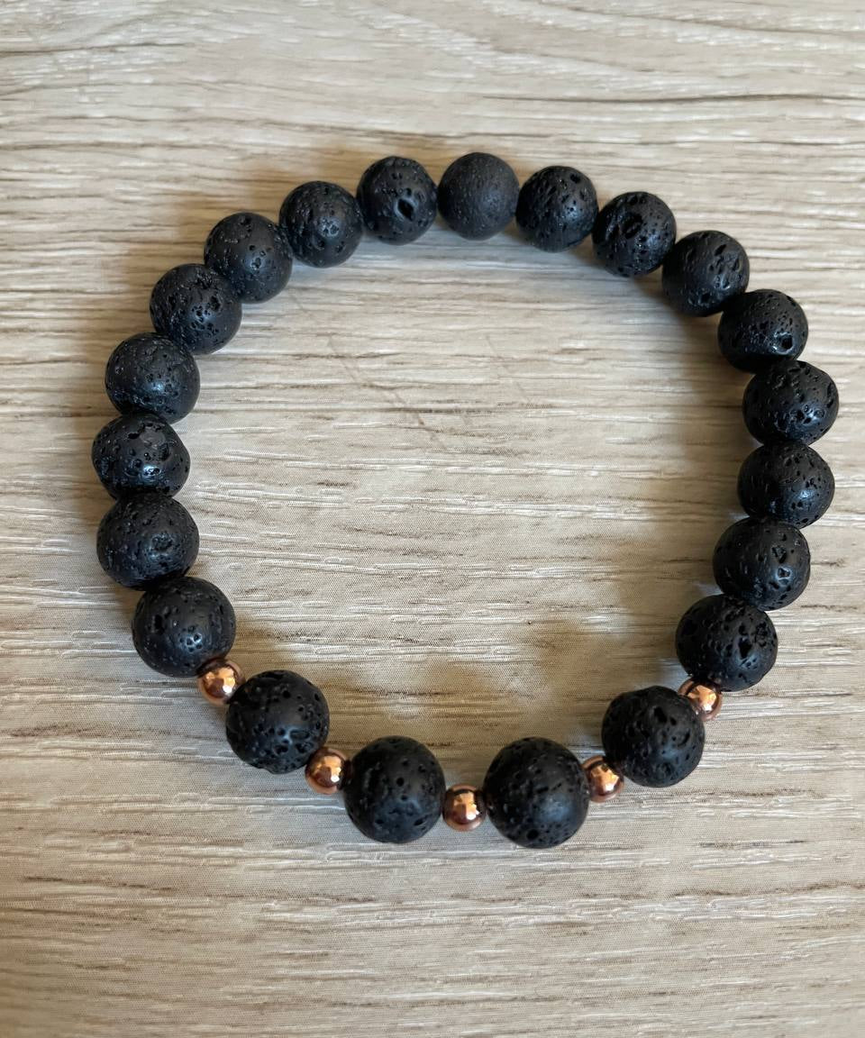 Lava stone bracelet with 5 rose gold beads against a wooden background.
