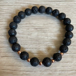 Lava stone bracelet with 5 rose gold beads against a wooden background.