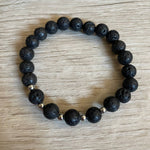 Lava stone bracelet with 5 silver beads against a wooden background.