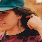 Woman in the desert wearing a blue cap and large wooden cactus earrings.