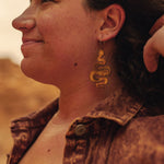 A woman in the desert wearing large wooden snake earrings.