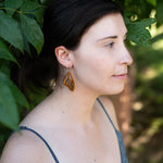 Woman wearing wooden butterfly earring looking off to the side with leaves in the background.