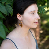 Woman wearing wooden butterfly earring looking off to the side with leaves in the background.