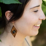 Woman wearing a decorative wooden earring with leaves in the background