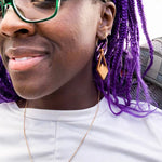 Woman with purple hair wearing diamond shaped wooden earrings with mountain peaks carved in the center.
