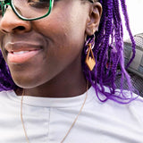Woman with purple hair wearing diamond shaped wooden earrings with mountain peaks carved in the center.