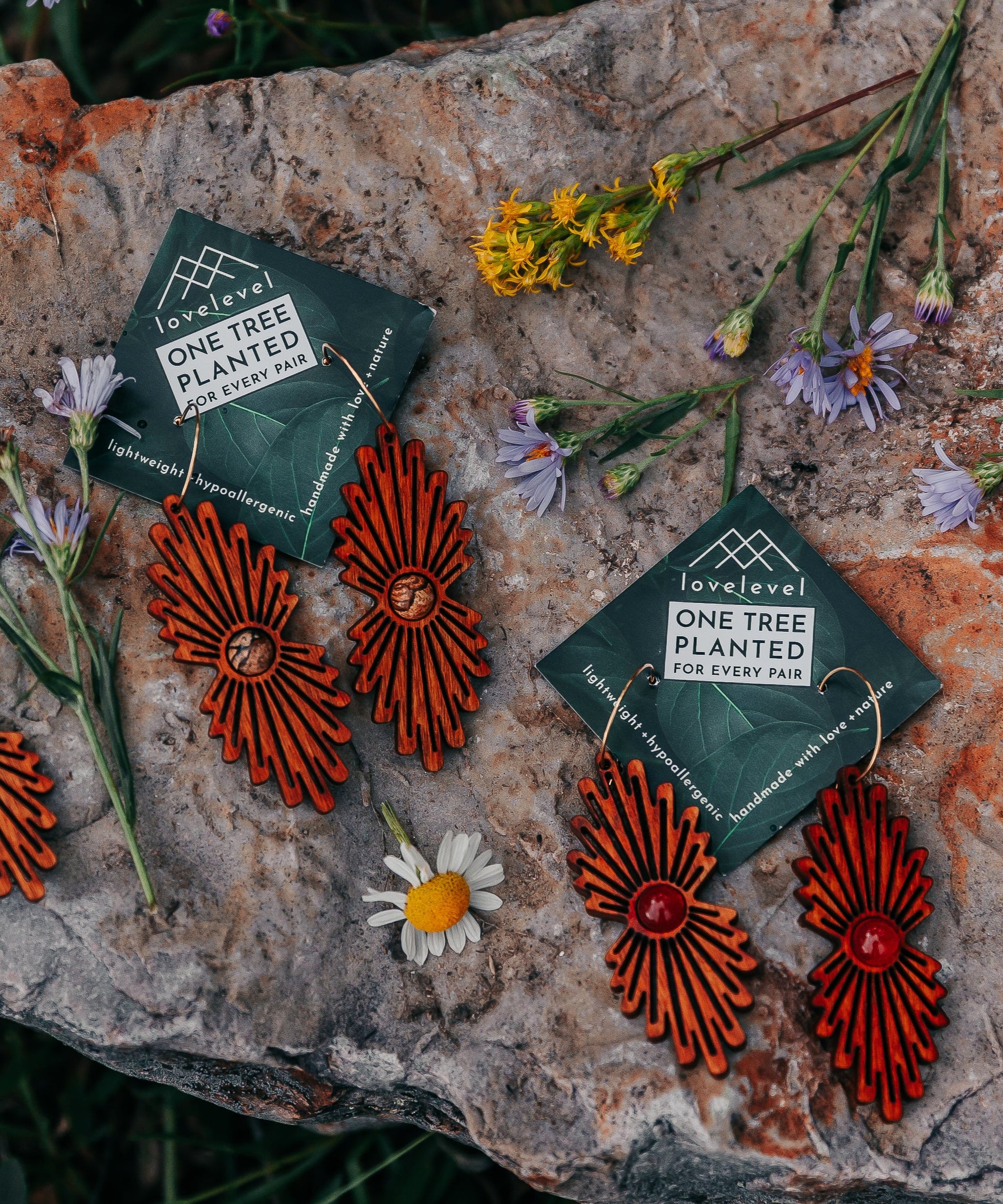 Wooden earrings with a stone center and carved ray bursts on a stone with wildflowers in the background