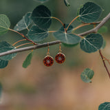 Pair of circular wooden earrings with an opaque stone in the center hanging from a stick with leaves.
