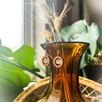 A pair of wooden earrings with a wood ring surrounding a small lotus charm hanging from the top of an orange glass vase.