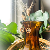 A pair of wooden earrings with a wood ring surrounding a small lotus charm hanging from the top of an orange glass vase.