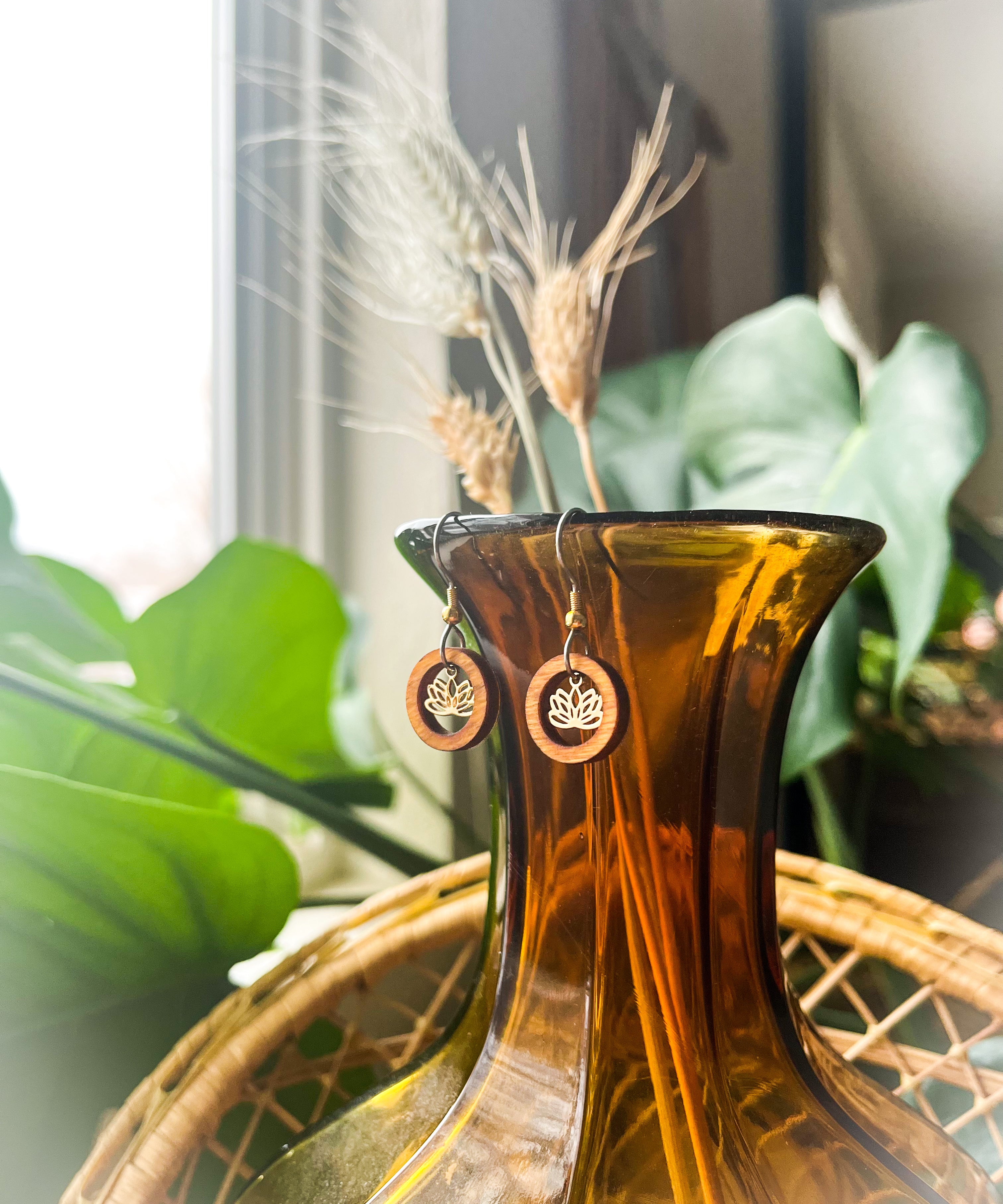 A pair of wooden earrings with a wood ring surrounding a small lotus charm hanging from the top of an orange glass vase.