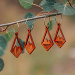 Two pairs of wooden diamond earrings with a mountain peak carved into the center, one with three slits cut out in the base of the mountain.
