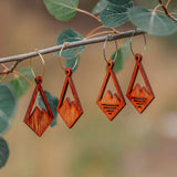 Two pairs of wooden diamond earrings with a mountain peak carved into the center, one with three slits cut out in the base of the mountain.