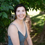 Smiling woman sitting under a tree wearing wooden earrings in the shape of butterfly wings.