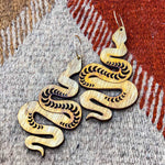 A pair of wooden snake earrings on top of a geometric carpet.
