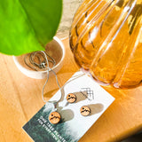 Wooden stud earrings with a mountain peak etched into them on a card with 'lovelevel' branding catching the sun underneath a leaf.