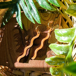 A pair of wooden earrings in a squiggle pattern among leaves in a whicker basket.
