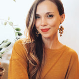 Smiling woman wearing wooden geometric earrings and a orange sweater.